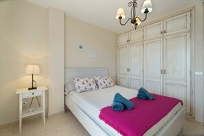 A bedroom with a bed, a nightstand, a lamp, a wardrobe, and a chandelier.