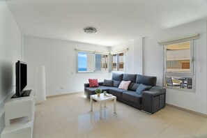 Una sala de estar moderna con un sofá gris, una mesa de centro blanca y un televisor de pantalla plana sobre un mueble blanco.