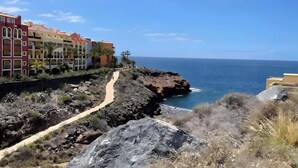 A coastal path leading to a rocky shoreline with buildings in the background.