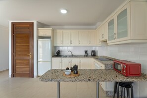 Una cocina con armarios blancos, microondas, cafetera y refrigerador.