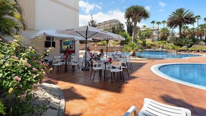 A poolside area with outdoor seating, palm trees, and a building with a sign. - Vacation 'The Dorado 206' with Shared Pool, Shared Terrace and Wi-Fi (Arona)