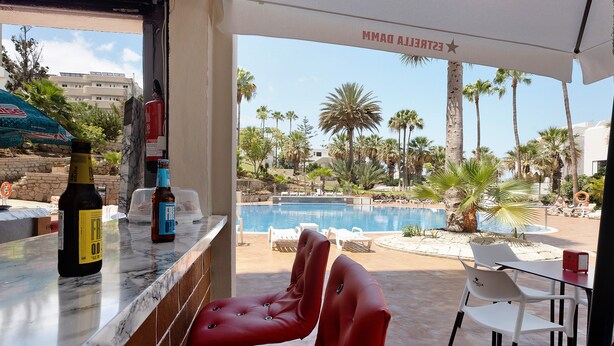 A bar area with a view of a pool and palm trees. - Vacation 'The Dorado 206' with Shared Pool, Shared Terrace and Wi-Fi (Arona)