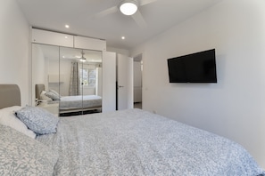 Une chambre à coucher comprenant un lit, un téléviseur fixé au mur, une armoire et un ventilateur de plafond.