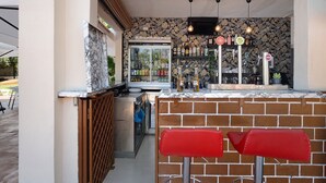 A bar area with a brick counter, two red bar stools, a refrigerator, and a patterned wall. - Vacation 'The Dorado 206' with Shared Pool, Shared Terrace and Wi-Fi (Arona)