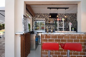 Un espace bar avec un comptoir en briques, deux tabourets de bar rouges, un réfrigérateur et un mur décoré de motifs.