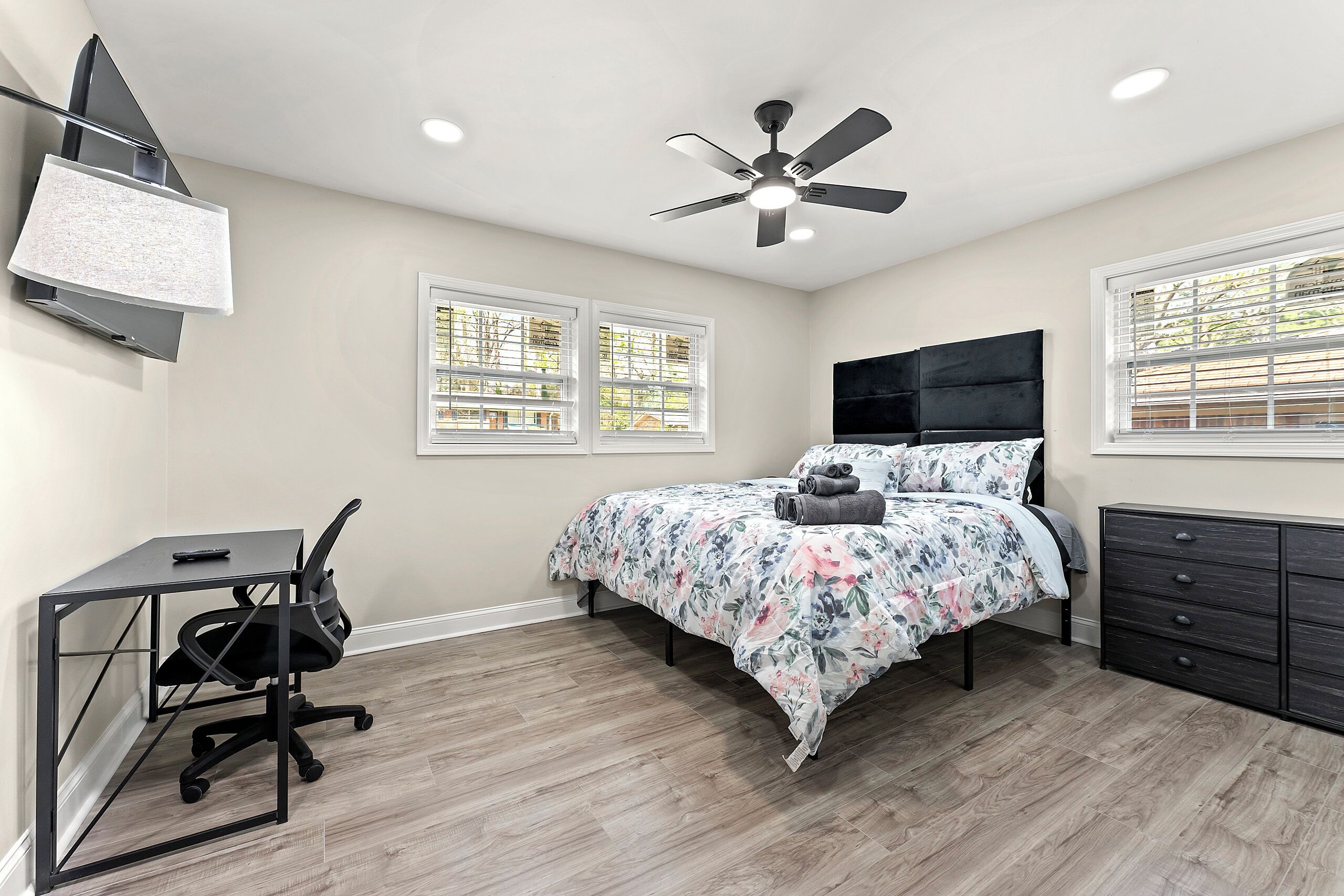 Une chambre à coucher comprenant un lit, un bureau, une chaise, un ventilateur de plafond et une commode.