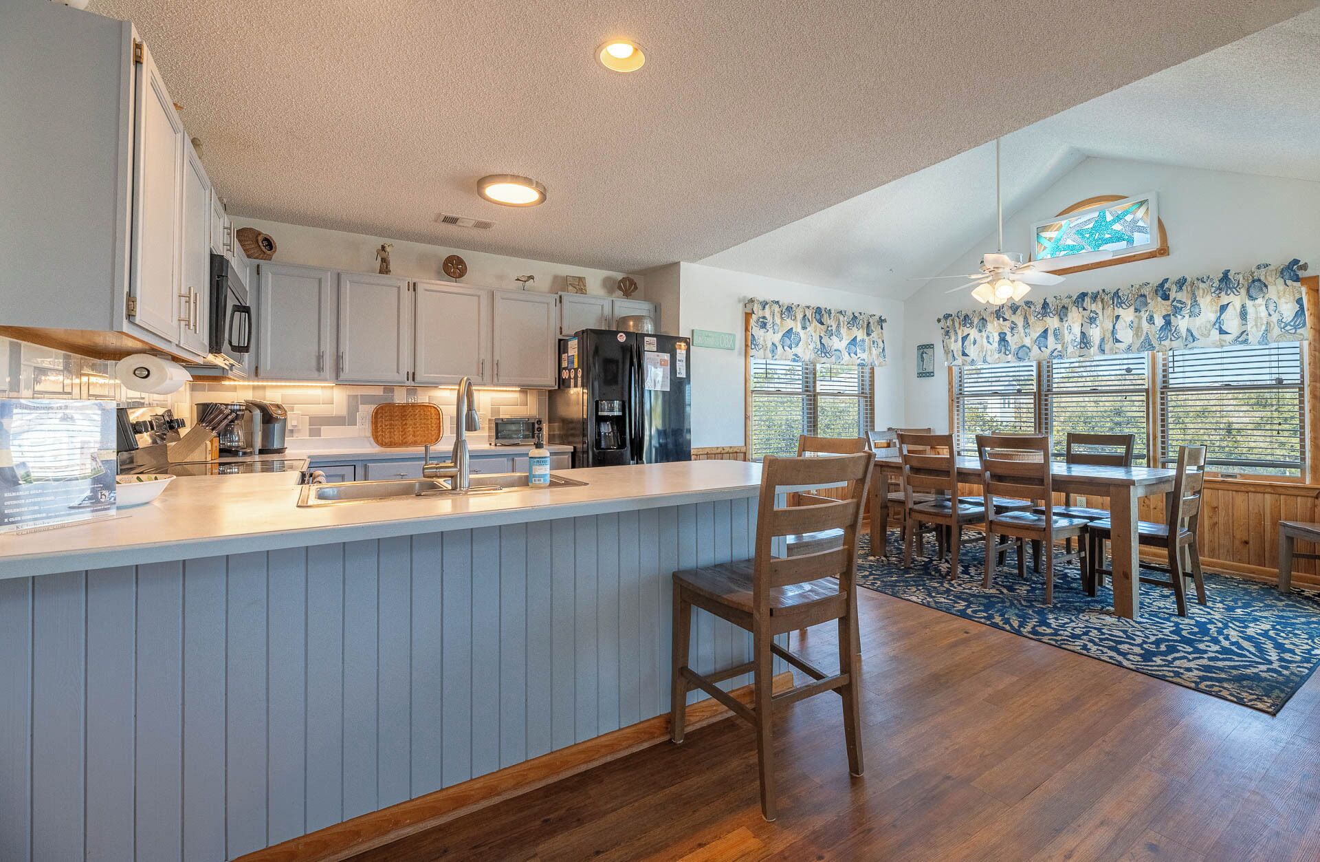 A kitchen with a wooden island, a dining area with a table and chairs, and a view of the outdoors through large windows.