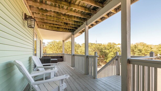 Eine überdachte Veranda mit weißen Holzstühlen und einer eingebauten Bank, mit Blick auf ein bewaldetes Gebiet.