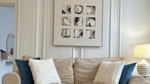 Uma sala de estar com um sofá bege, uma mesa de centro e uma obra de arte abstrata emoldurada na parede.