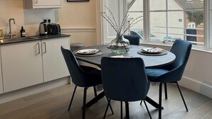 Uma cozinha moderna com armários brancos, uma mesa de jantar com cadeiras azuis e uma janela grande que oferece vista para o exterior.