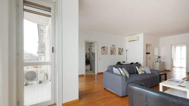 A spacious living area with a grey sofa, a white coffee table, and a large window.