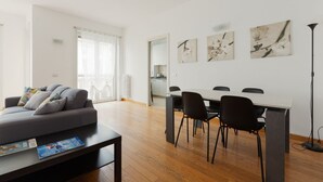 A modern living room with a sofa, a dining table with chairs, and artwork on the wall.