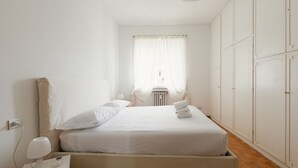 A bedroom with a bed, bedside tables, a lamp, a radiator, and a wardrobe.