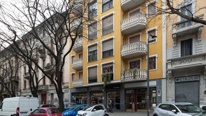 A multi-story yellow building with balconies, parked cars, and a storefront with signage.