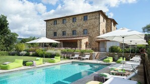 A stone building with a swimming pool, green lounge chairs, and umbrellas. - Villa Piandolce - Radda In Chianti (SI)