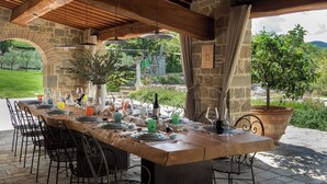 An outdoor dining area with a stone table, metal chairs, and a view of greenery and hills. - Villa Piandolce - Radda In Chianti (SI)