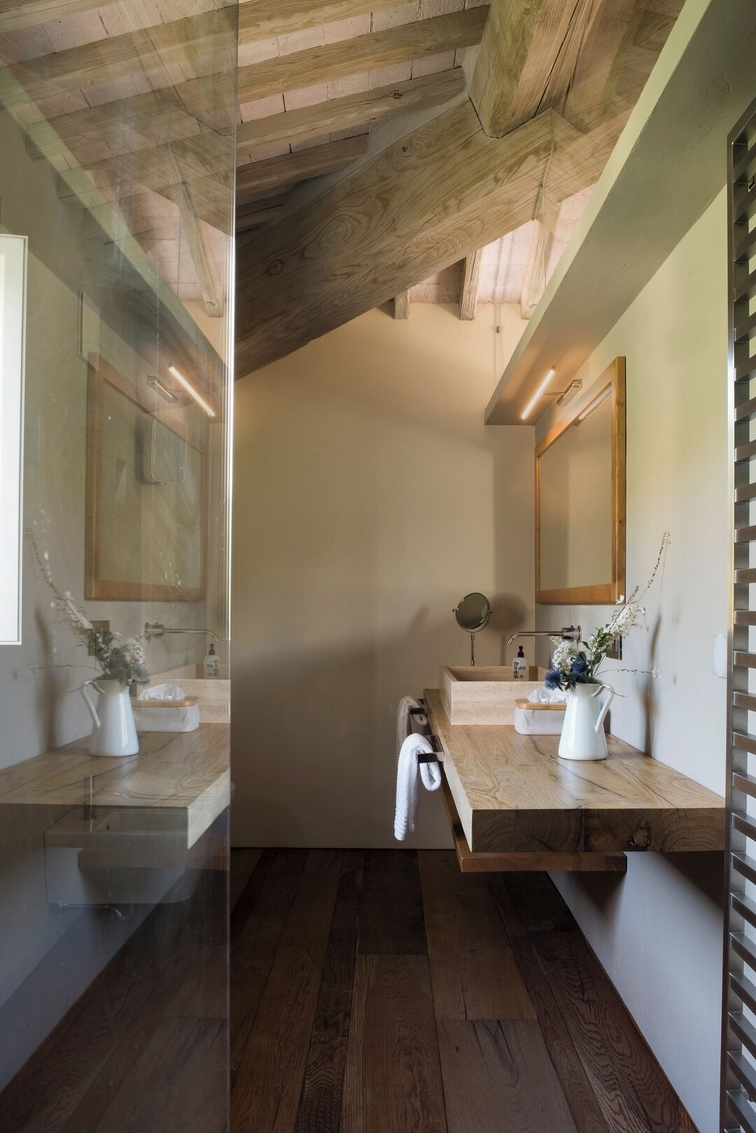 Une salle de bain moderne avec des poutres en bois, un grand miroir et deux vasques dotées de robinetterie blanche.