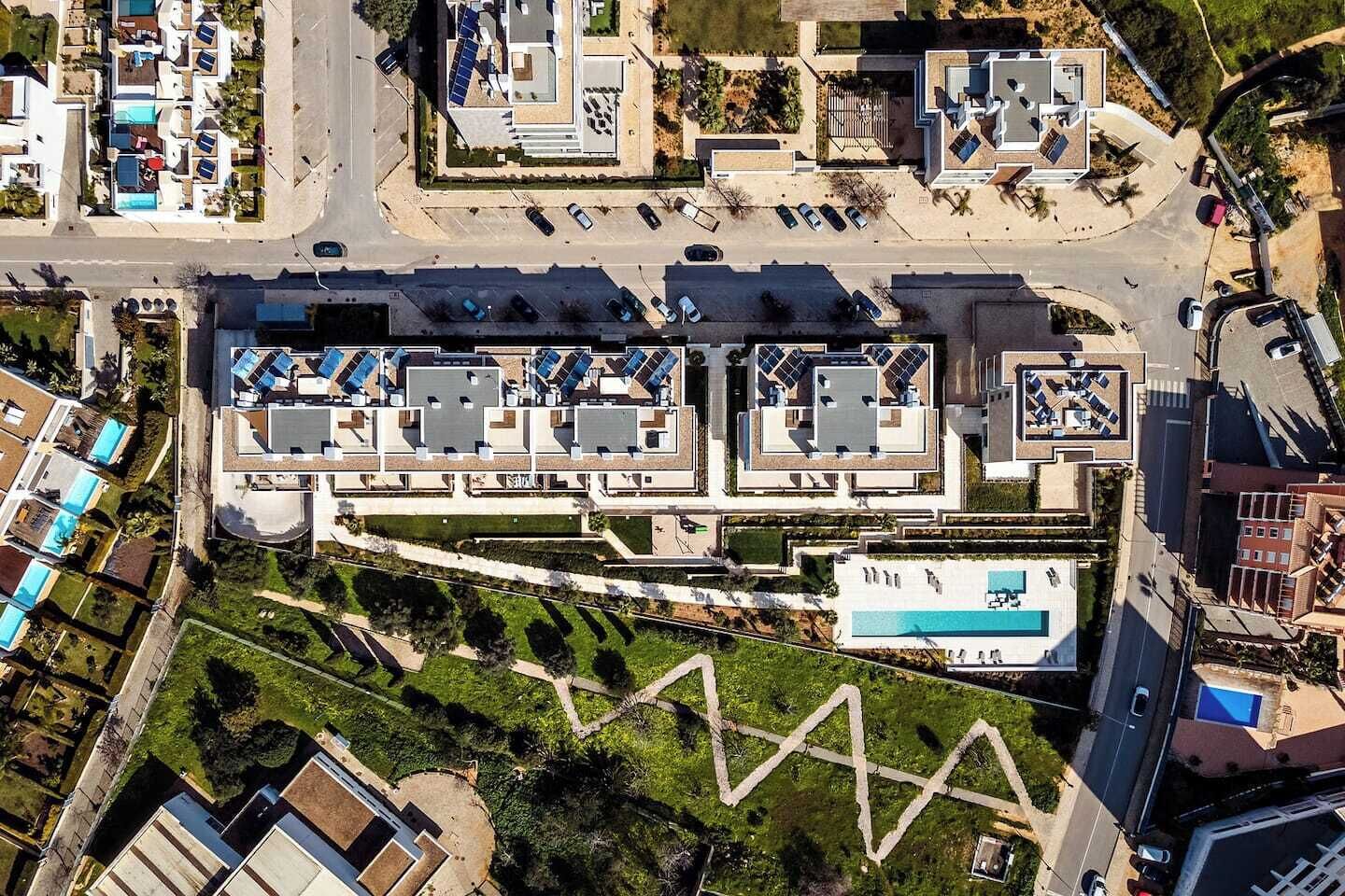 Eine Vogelperspektive eines modernen Hotels mit mehreren Dachpools, einem zentralen Innenhof und einem Schwimmbecken.