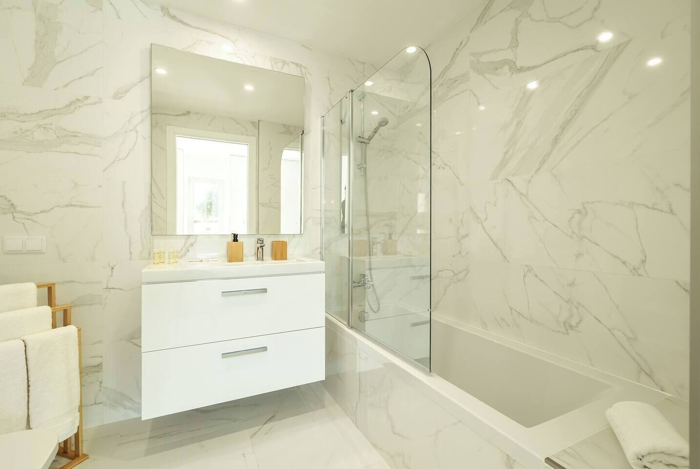 A modern bathroom with a marble floor, a glass shower enclosure, and a white vanity with drawers.