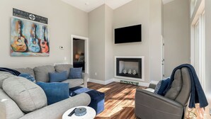 Un salon moderne avec un canapé gris, des coussins bleus, un fauteuil gris, une cheminée et un tableau représentant des guitares.