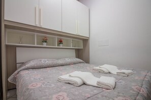 A bedroom with a bed, a headboard, a wardrobe, and a shelf with decorative items.