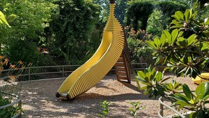 Une aire de jeux avec un toboggan jaune et une structure d’escalade en bois.