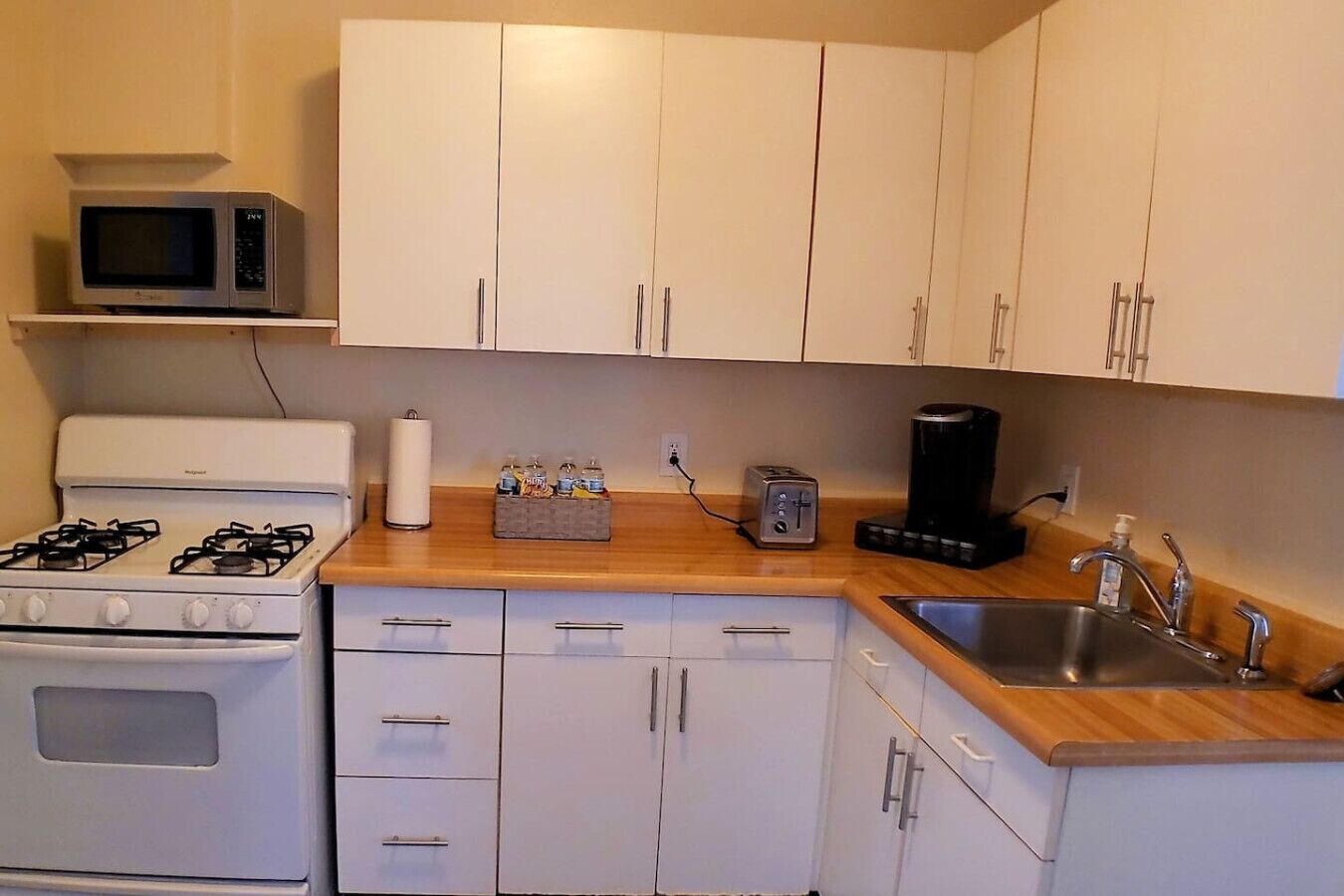 Uma cozinha compacta com armários brancos, fogão a gás, micro-ondas, torradeira e cafeteira.