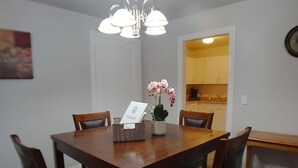 Une salle à manger avec une table en bois, quatre chaises, un vase de fleurs roses et une pancarte de bienvenue.