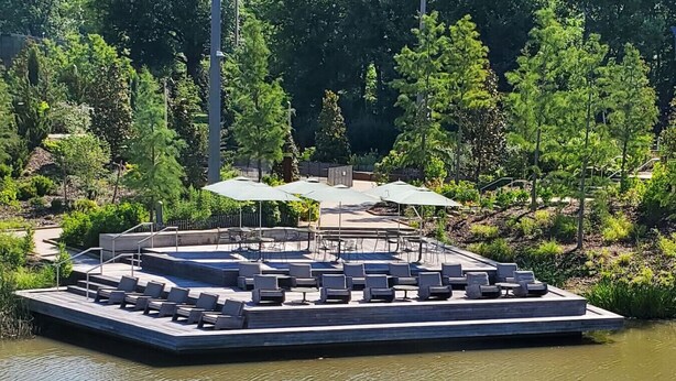 Une terrasse au bord du lac, dotée de chaises longues et de parasols, et entourée d’arbres.