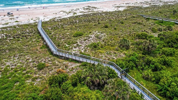 Une route côtière avec un pont reliant deux zones, bordée de verdure et menant à une plage.