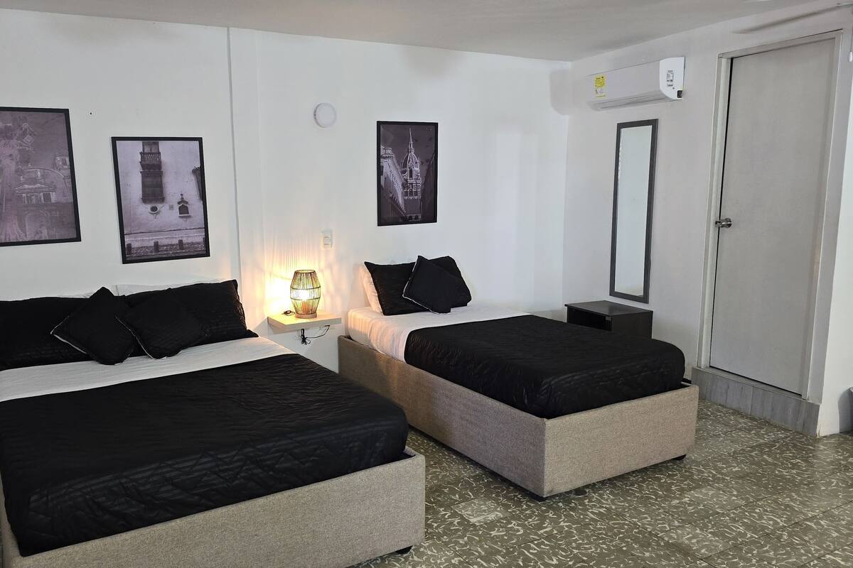 A hotel room with two beds, a nightstand with a lamp, and a door.