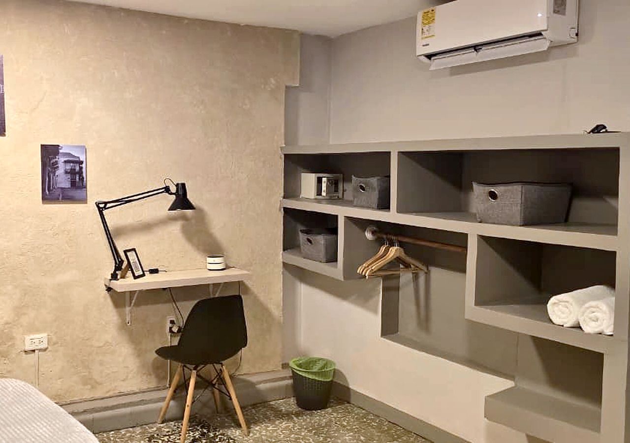 A bedroom with a desk, chair, shelves, and an air conditioning unit.