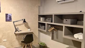 A bedroom with a desk, chair, shelves, and an air conditioning unit.