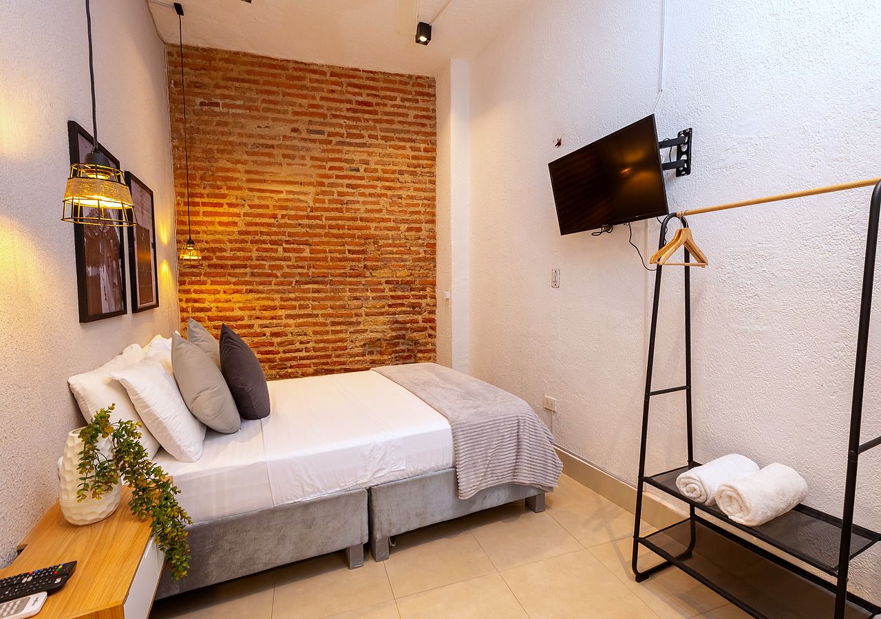 Une chambre moderne avec un mur en briques, un lit, une télévision et une étagère avec des serviettes.