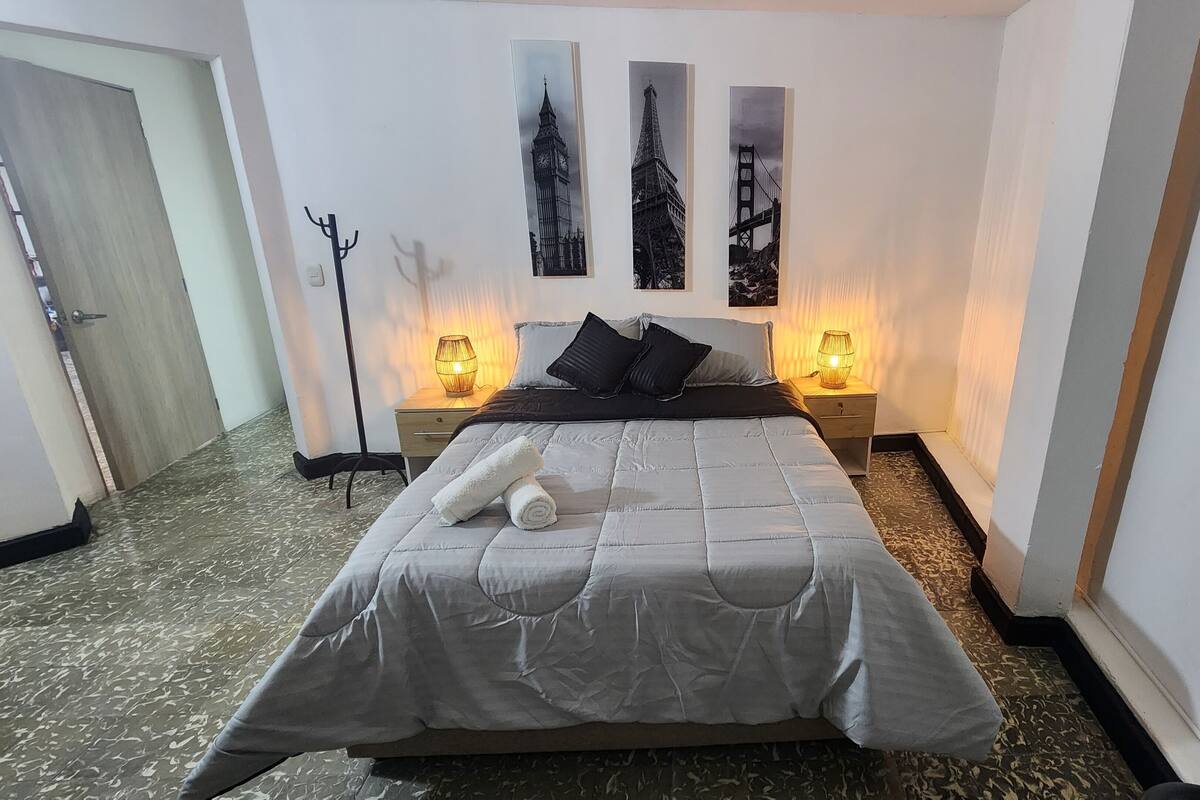 A neatly made bed with a grey duvet, two bedside lamps, and three framed pictures on the wall.