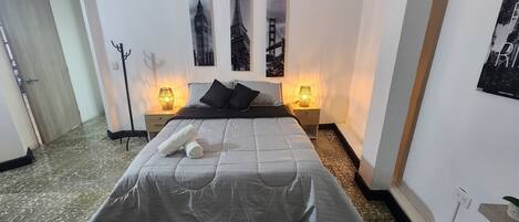 A neatly made bed with a grey duvet, two bedside lamps, and three framed pictures on the wall.