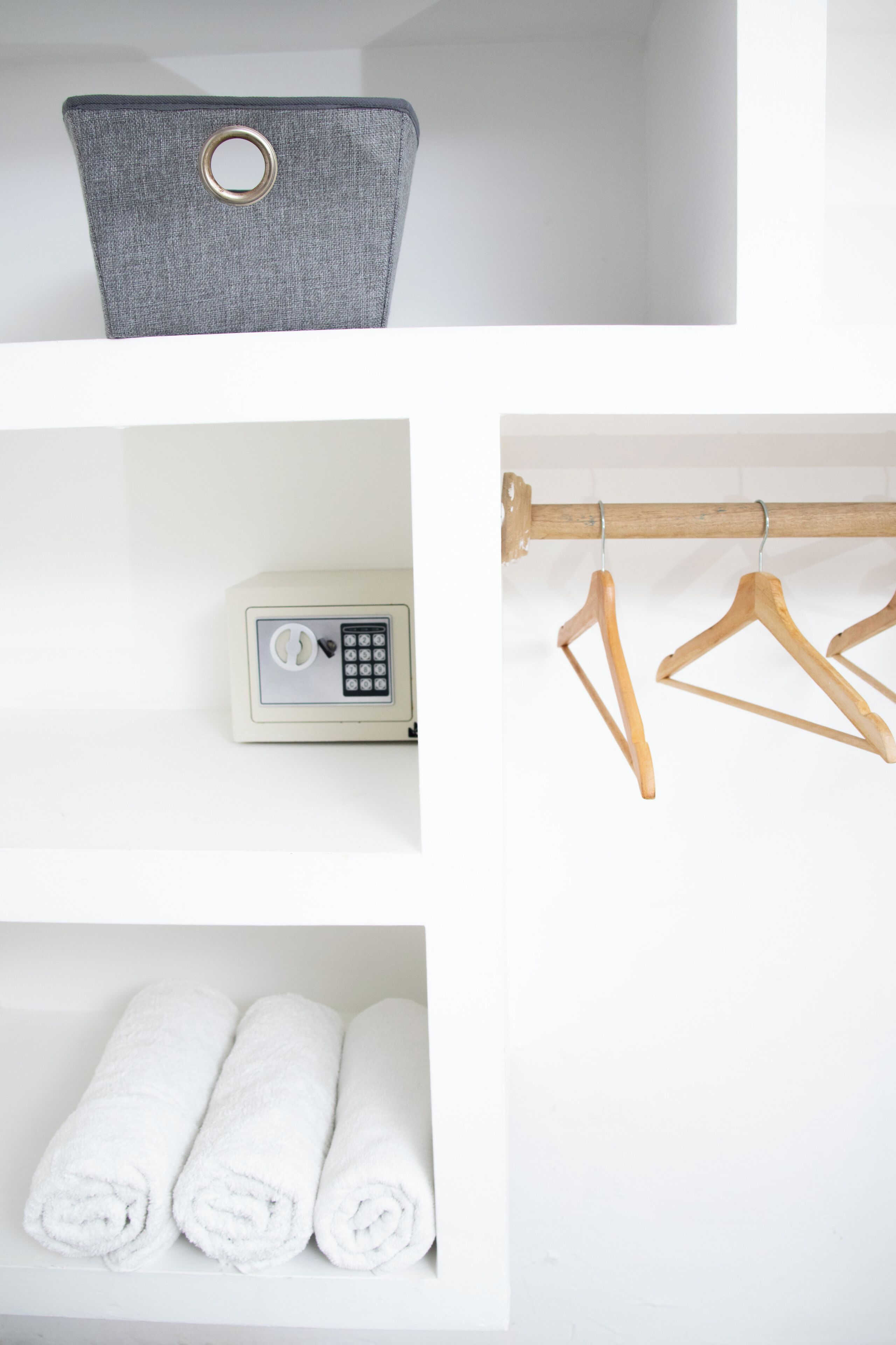 A storage unit with a grey fabric cover, a small electronic device, wooden hangers, and neatly rolled white towels.