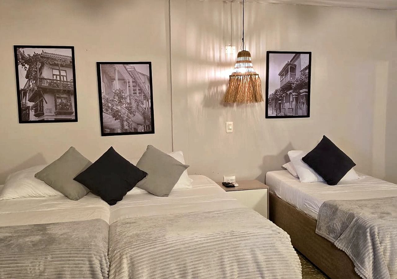 A hotel room with two beds, a chandelier, and three black-and-white photographs on the walls.