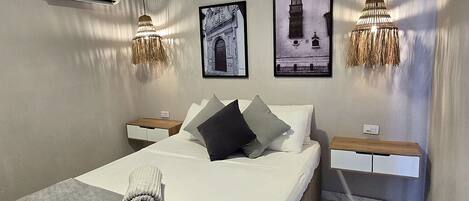 Une chambre à coucher comprenant un lit, deux tables de chevet, un climatiseur fixé au mur et deux lampes suspendues.