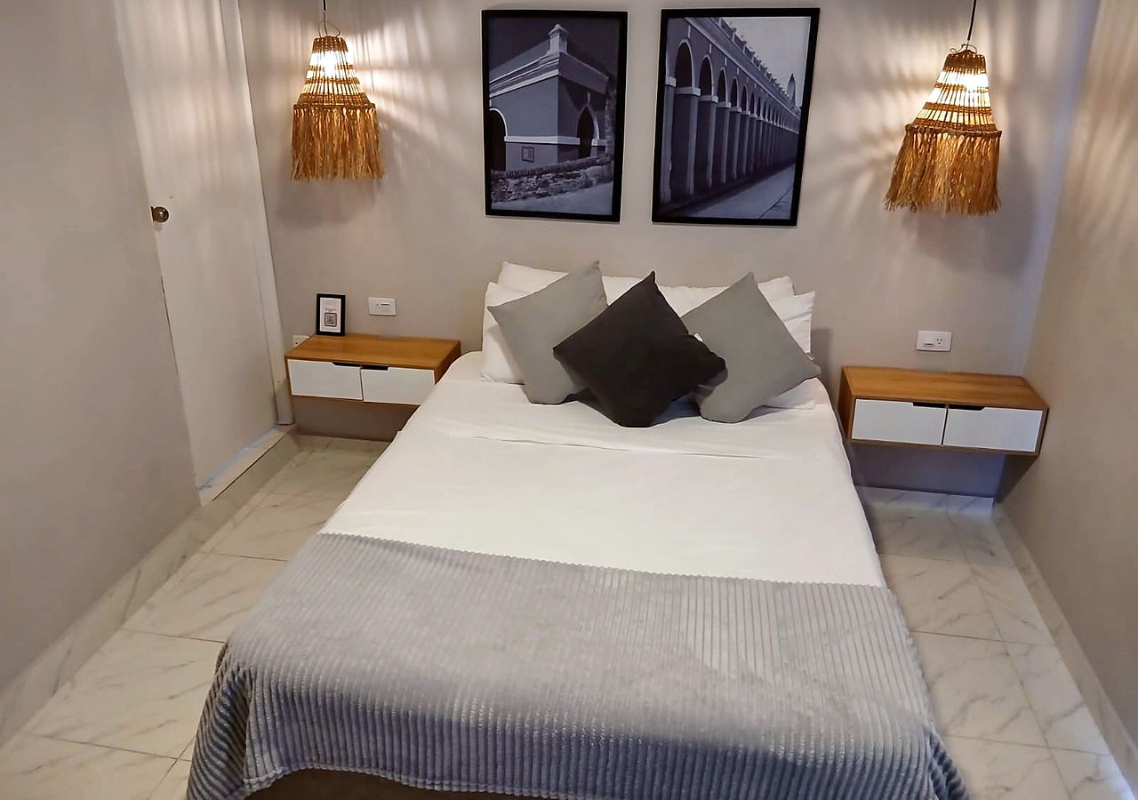 A bedroom with a bed, two nightstands, a bedside table, a lamp, and two framed pictures on the wall.