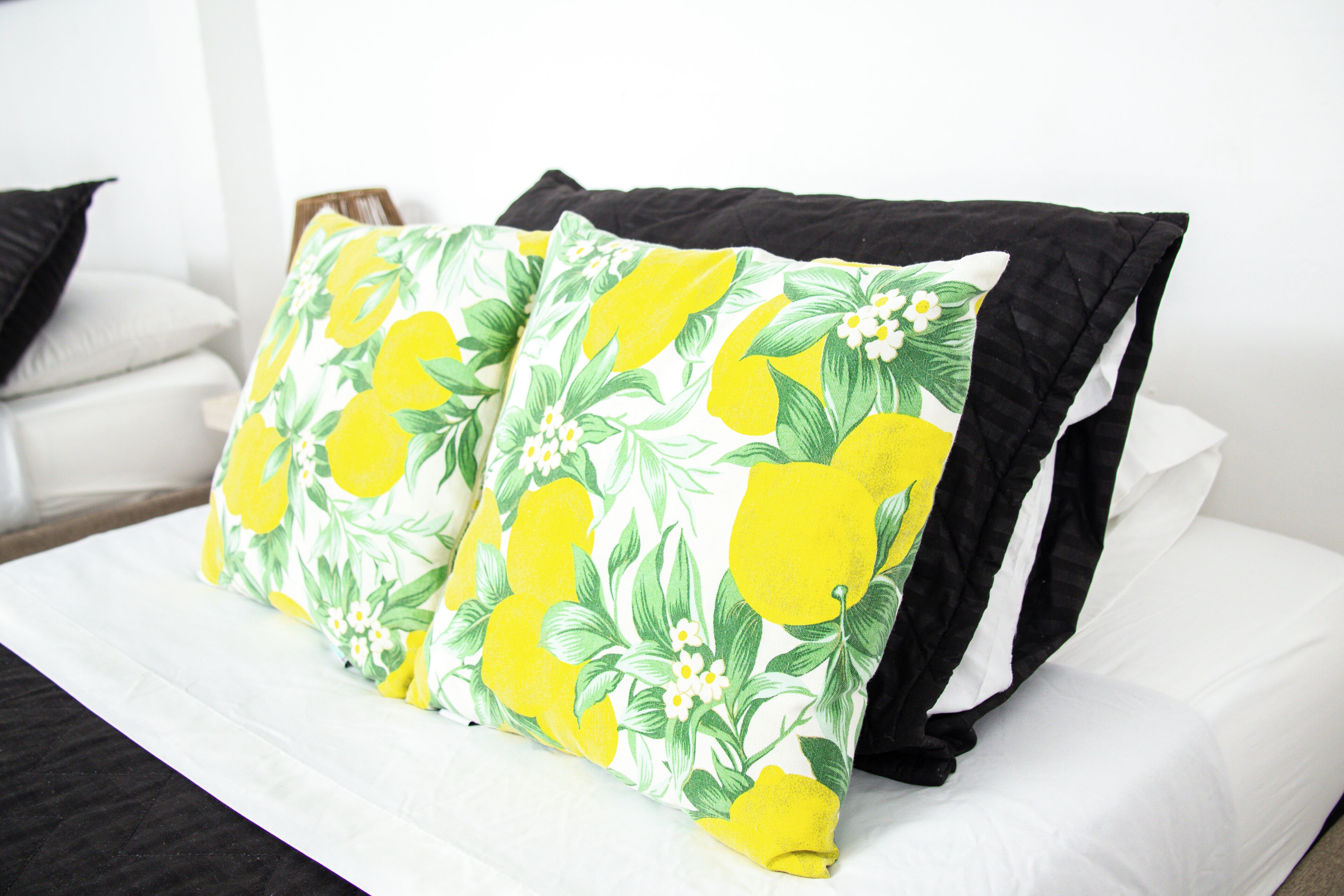 A bed with white bedding and two pillows, one with a floral pattern and the other plain black.