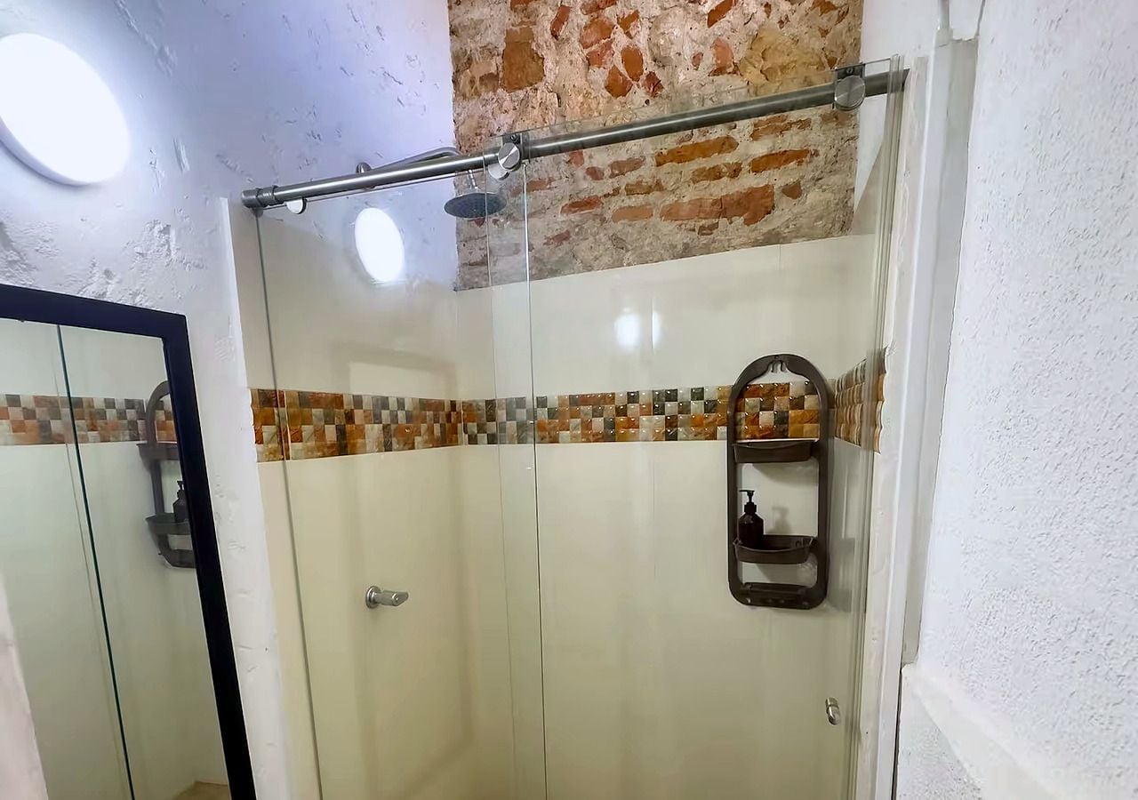 Ducha con mampara de vidrio, pared de azulejos y estante metálico.