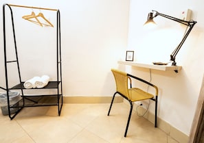 A room with a black metal shelf unit holding towels, a wicker chair, a desk with a lamp, and a small framed picture. - Hotel Casa Agena (Cartagena)