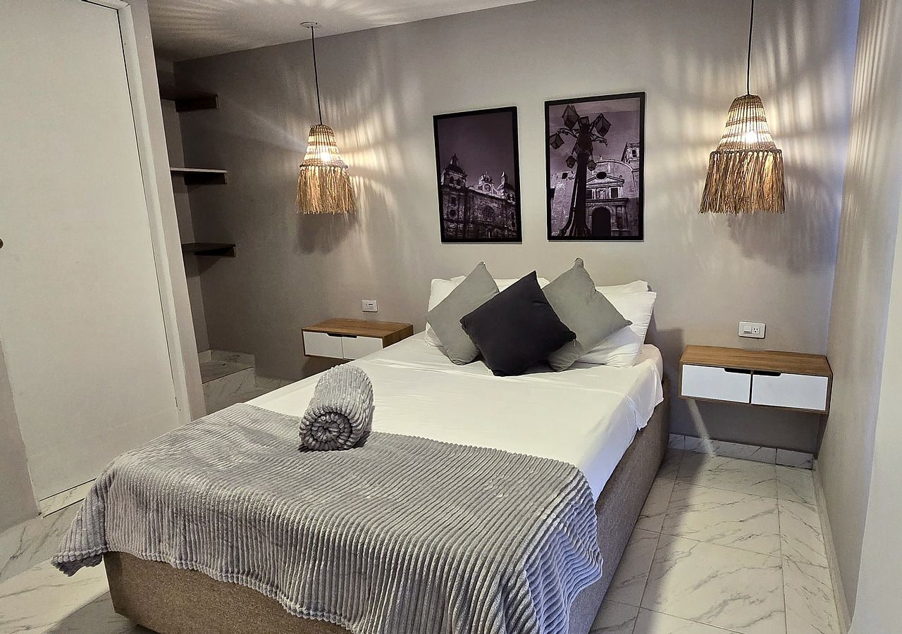A bedroom with a bed, bedside tables, a hanging light fixture, and two framed pictures on the wall.