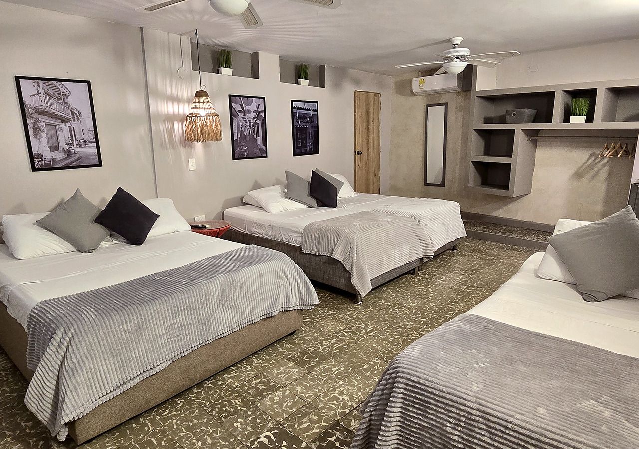 A hotel room with three beds, a ceiling fan, wall-mounted shelves, and framed pictures.