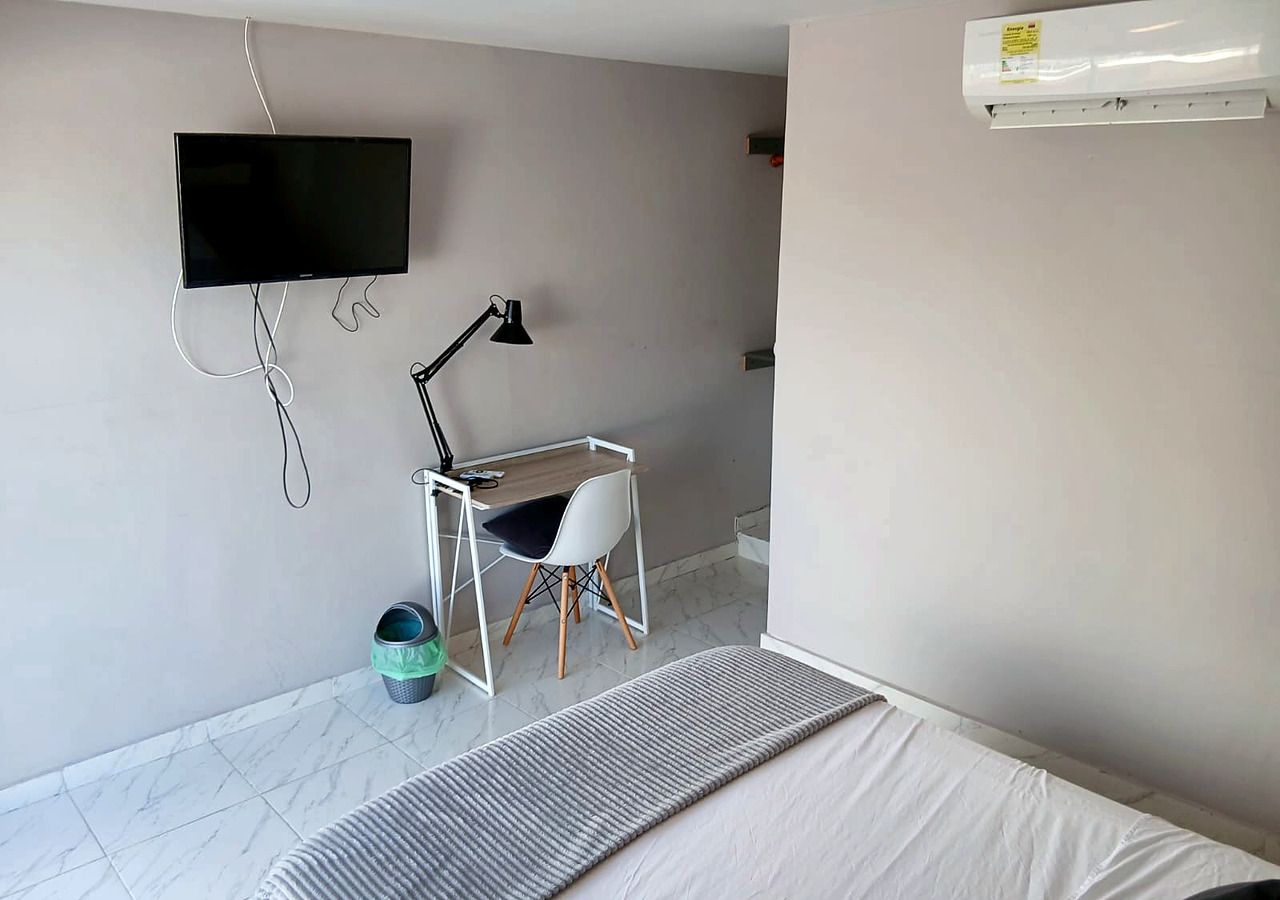 A bedroom with a bed, a desk, a chair, a television, and an air conditioning unit.