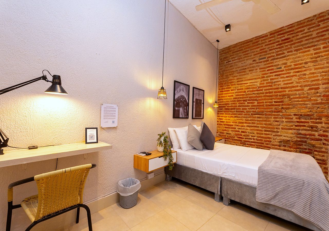 A compact room with a bed, a desk, a chair, and a small trash bin.