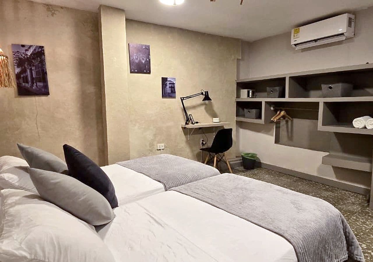 A bedroom with two beds, a desk, and a chair. There is an air conditioning unit on the wall.