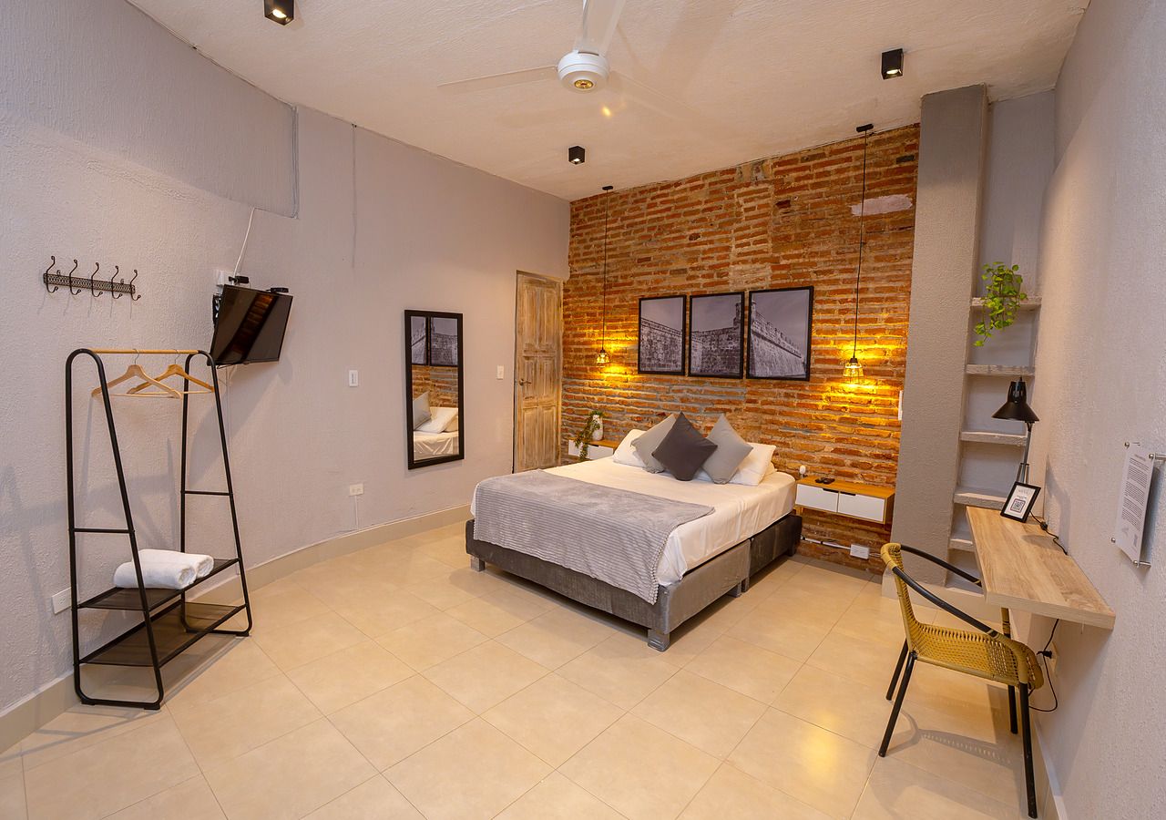 A modern bedroom with a bed, a wooden desk, a chair, a hanging light fixture, and a brick wall.