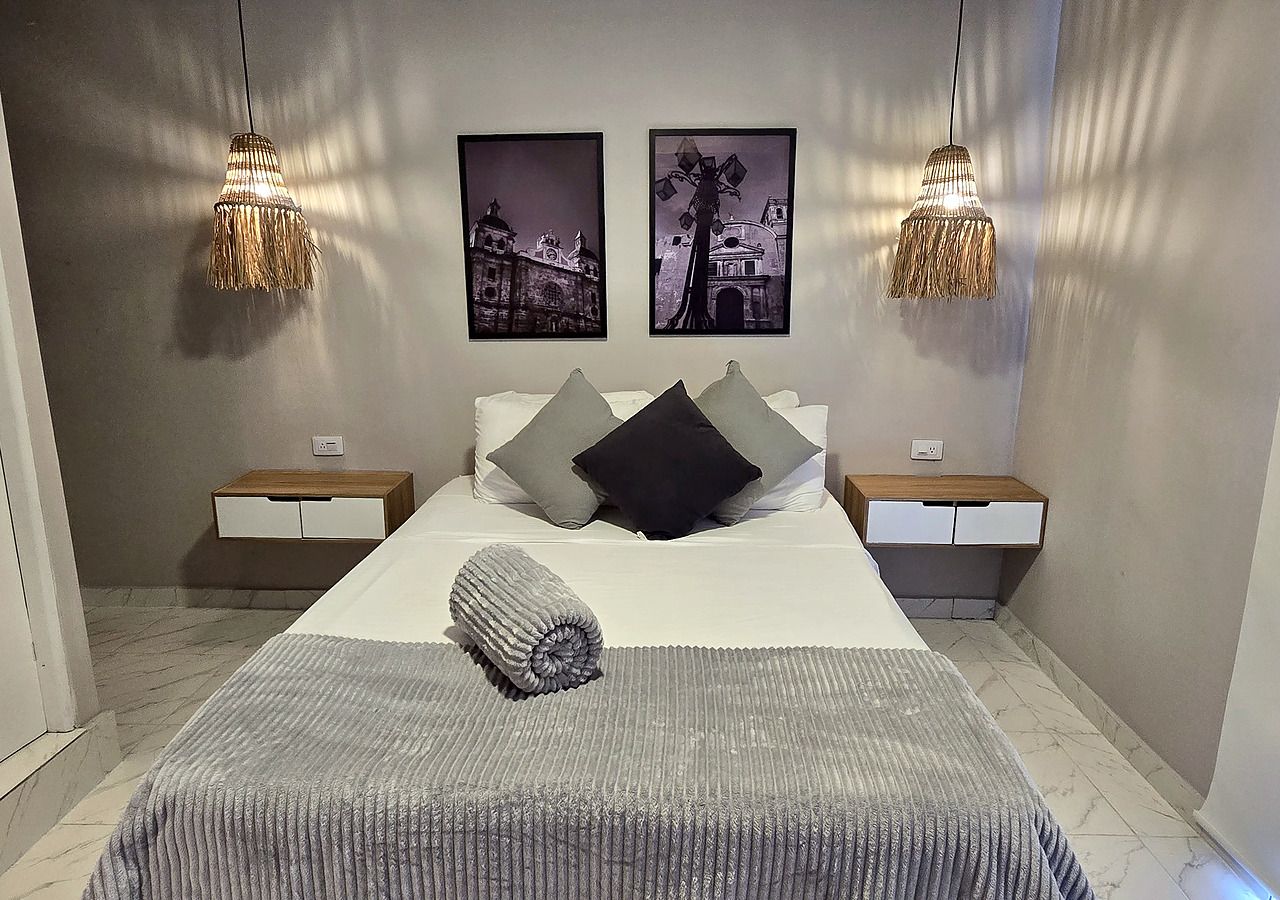 A modern bedroom with a large bed, two nightstands, a bedside table, a rolled towel, and two wall-mounted lamps.